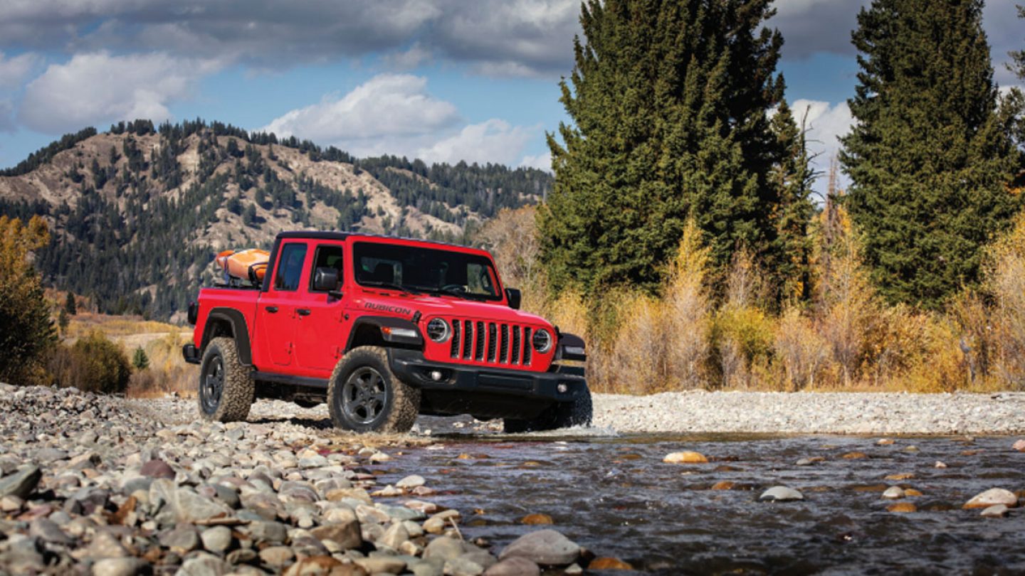 Red Gladiator parked beside a rocky stream 